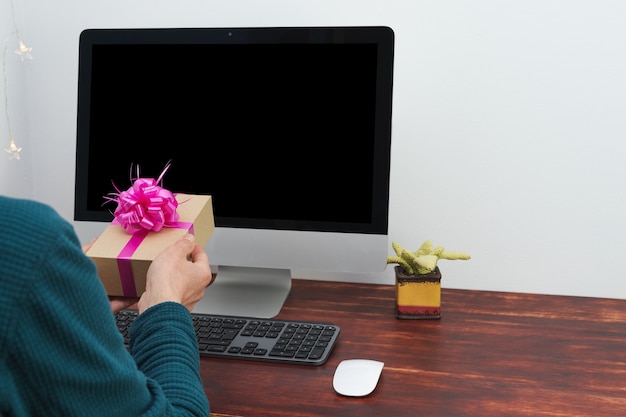 Virtual gift exchange. Man offering gift in front of computer. Moc. Virtual Valentine's Day. Mockup black screen.