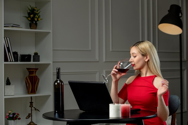 Amore virtuale ragazza bionda carina in abito rosso in data a distanza con vino che beve dal vetro