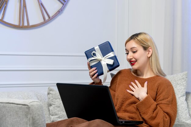 Amore virtuale ragazza bionda carina in maglione accogliente sulla data di distanza del computer che tiene presente