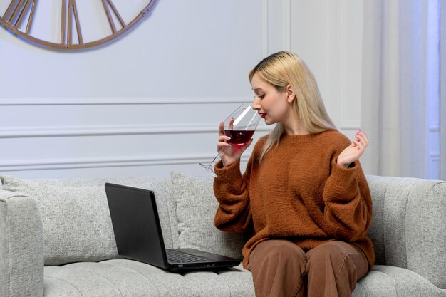 레드 와인을 마시는 원격 컴퓨터 날짜에 아늑한 스웨터에 가상 사랑 귀여운 젊은 금발 소녀