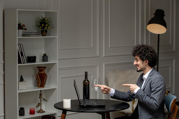 Virtual love handsome cute guy in a suit with wine on a distance computer date pointing at screen