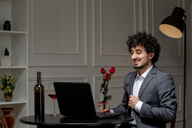 Virtual love handsome cute guy in suit with wine on a distance computer date red roses in hands