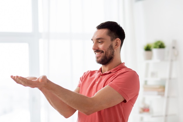 virtual reality, entertainment and people concept - happy man holding something imaginary on palms at home