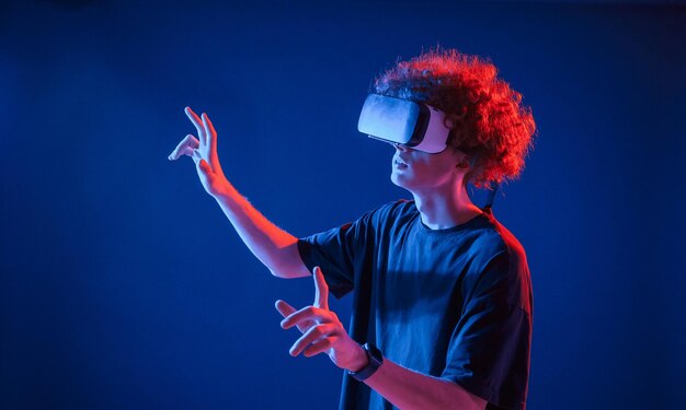 Virtual reality experience young man with curly hair is indoors illuminated by neon lighting