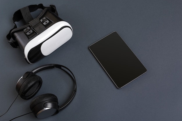 Virtual reality glasses and tablet with headphones on a gray background top view