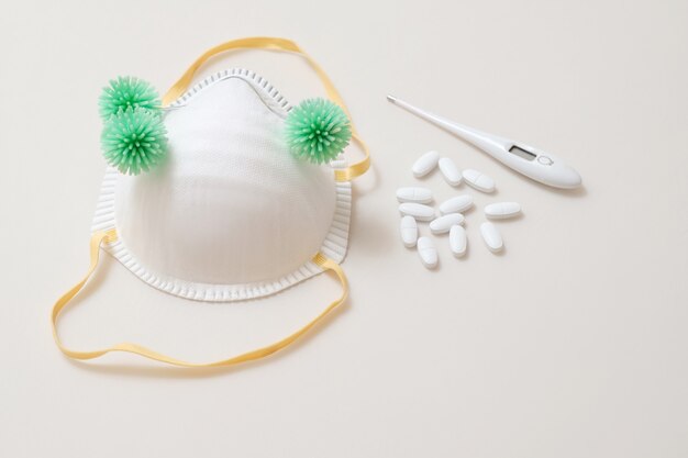 Virus on medical mask with thermometer and pills on the table