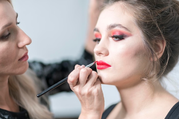 Visagist brengt rode lippenstift aan Mooi vrouwelijk gezicht Sensuele lippen Make-up in uitvoering