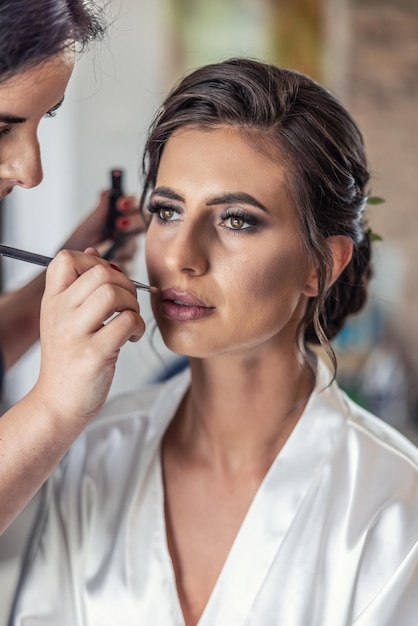 Visagist die make-up aanbrengt op een gezicht van een mooie bruid