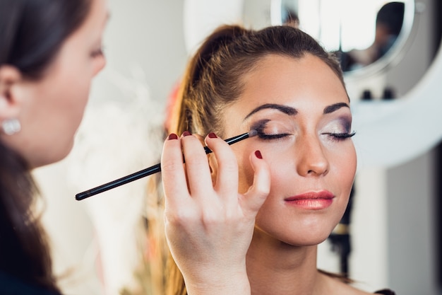 Visagist doet professionele make-up van mooie jonge vrouw.