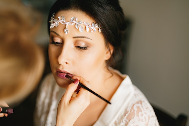 Visagist maakt make-up voor de bruid in een hotelkamer tijdens de voorbereiding op de huwelijksceremonie