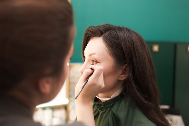 Visagist zet oogschaduw op een jong mooi meisje. Mooie dame kwam naar een schoonheidssalon voor cosmetische ingrepen