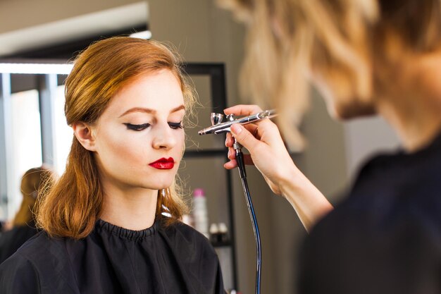 Visagiste maakt het meisje professionele make-up met een airbrush. Een close-up shot.