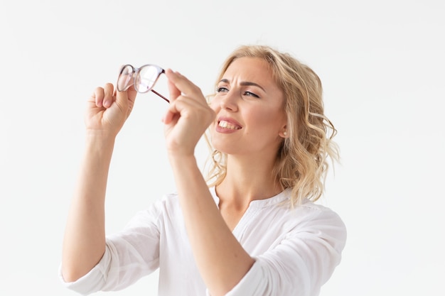 Visie, optica en schoonheid - Jonge blonde vrouw die een bril op een witte muur zet.