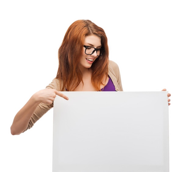 vision, health, advertisement and people concept - smiling girl wearing eyeglasses pointing finger to white blank board