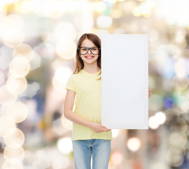 vision, health, advertisement and people concept - smiling little girl wearing eyeglasses with white blank board