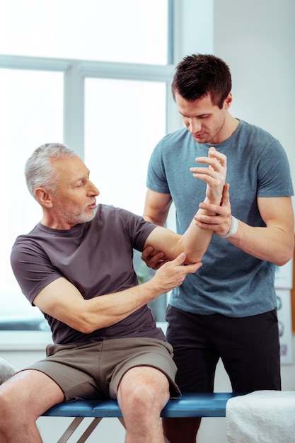 Visit to the hospital. Nice elderly man holding his hand up while describing his problem to the doctor