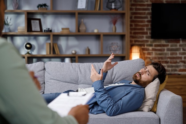 Photo visit to a psychologist a handsome man is lying on the couch and talking to a psychotherapist the pa