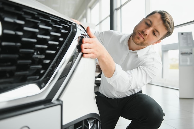 Foto in visita alla concessionaria di automobili bell'uomo barbuto sta accarezzando la sua nuova auto e sorridendo