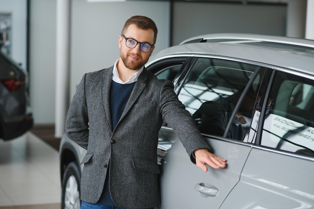 Visiting car dealership Handsome bearded man is stroking his new car and smiling