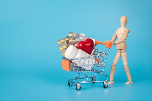 Visiting online drug store concept. Photo of wooden mannequin carrying holding push cart full of medicament isolated blue background with space for text