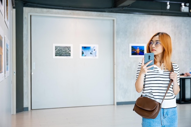 Visitor woman standing takes picture art gallery collection in front framed paintings pictures