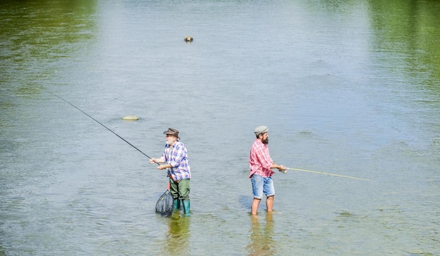 Vissen is veel meer dan vis Mannelijke vriendschap Vader en zoon vissen Zomerweekend Vrolijke visser met hengel en net Hobby- en sportactiviteit Samen vissen Mannen staan in het water