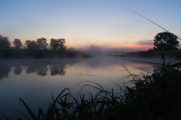 Vissen op mistig meer in de vroege ochtend net voor zonsopgang.