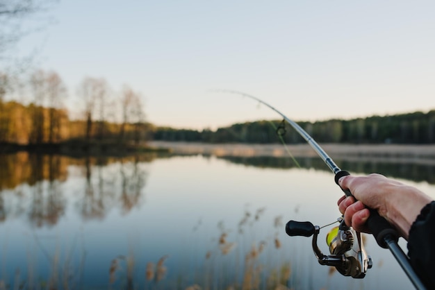 Visser met hengel draaiende haspel op de oever van de rivier Zonsopgang Vissen op snoekbaars karper Mist tegen de achtergrond van de achtergrond van het meer Mistige ochtend wilde natuur Het concept van een landelijke vakantie