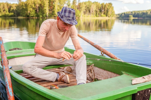 Visser met hengels is vissen in een houten boot tegen de achtergrond van prachtige natuur en meer of rivier. Camping toerisme ontspannen reis actieve levensstijl avontuur concept