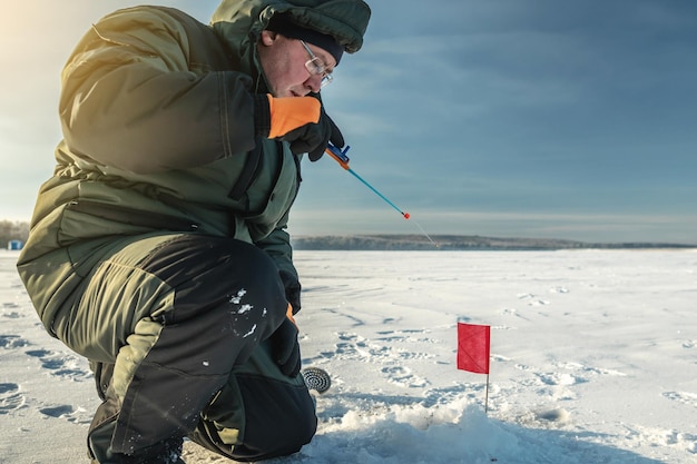 Visser vist in een gat op een groot bevroren meer op een zonnige dag de vreugde van wintervissen