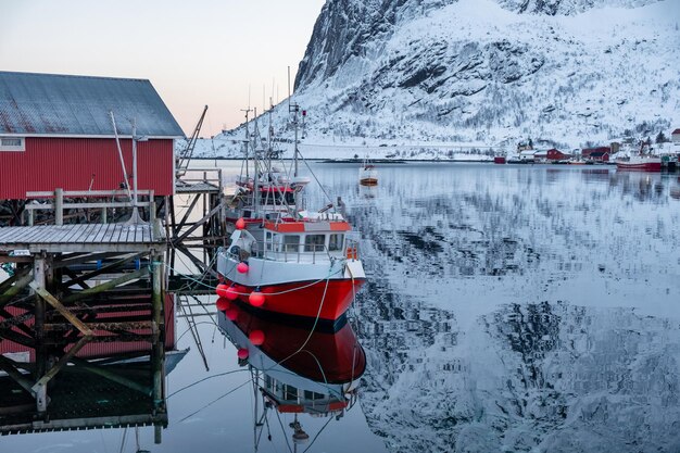 Visserijboot verankerd op een pier met een rood dorp op de Lofoten-eilanden