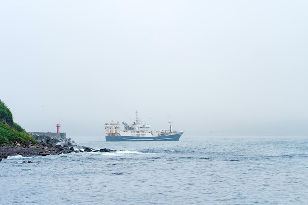 Vissersvaartuig komt tevoorschijn van achter een kaap met een vuurtoren die in een mistige zee vaart