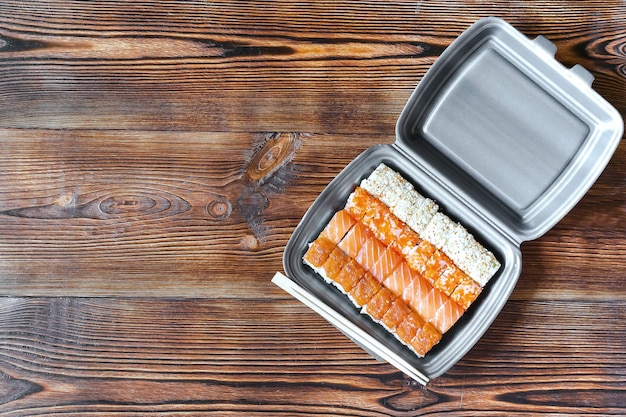 Vissushibroodjes met zalm en sesam verpakt in wegwerpvoedselcontainer. Zeevruchten, Thuisbezorging eten