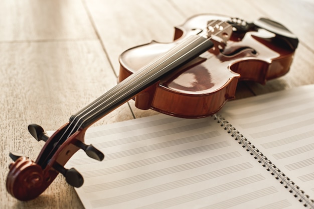 Visual beauty of classical instrument. Close up view of brown beautiful violin lying on sheets for music notes over wooden floor. Musical instruments. Music equipment. Music background