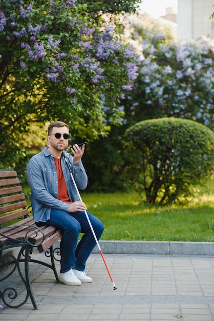 Visually impaired man with walking stick sitting on bench in city park Copy space