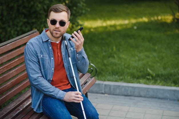 Visually impaired man with walking stick sitting on bench in city park Copy space