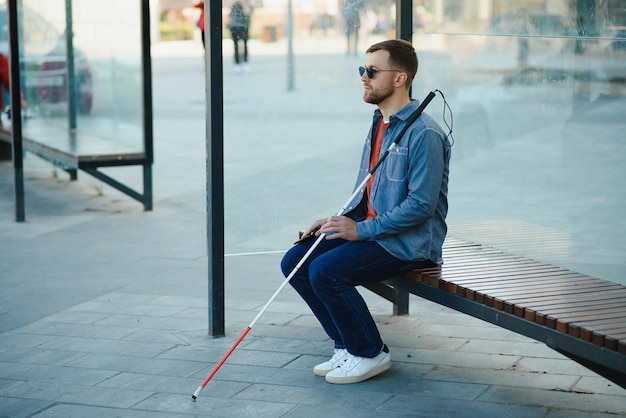 Visually impaired man with walking stick sitting on bench in city park Copy space