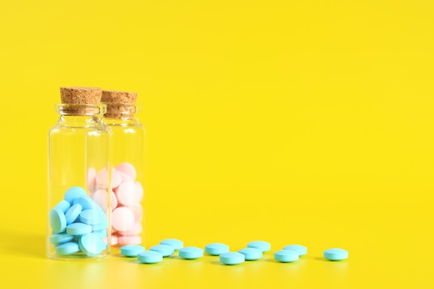 Vitamin B complex A set of blue and pink pills in glass bottles on a yellow background Health care