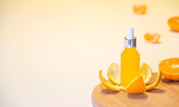 Vitamin C serum cosmetic bottle in tangerine peel with orange pieces on white background with copy space.