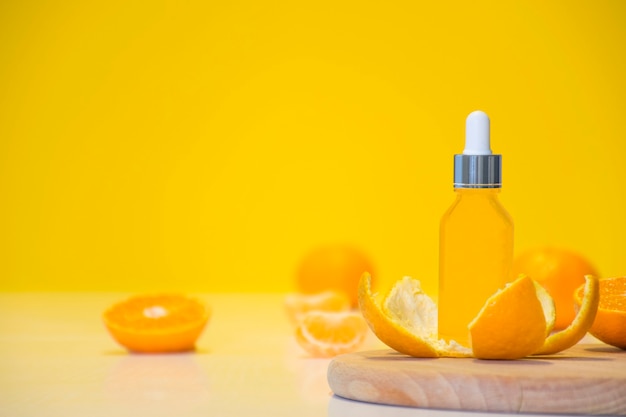 Vitamin c serum cosmetic bottle in tangerine peel with orange pieces on yellow background with copy space