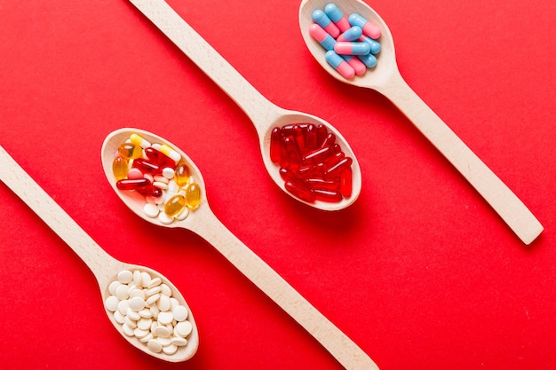 Vitamin capsules in a spoon on a colored background Pills served as a healthy meal Red soft gel vitamin supplement capsules on spoon
