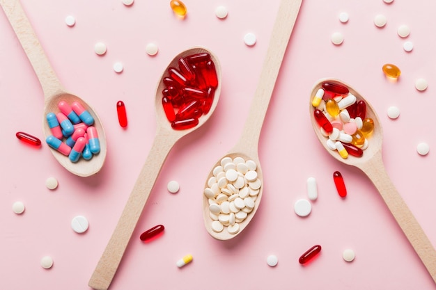 Vitamin capsules in a spoon on a colored background pills\
served as a healthy meal red soft gel vitamin supplement capsules\
on spoon