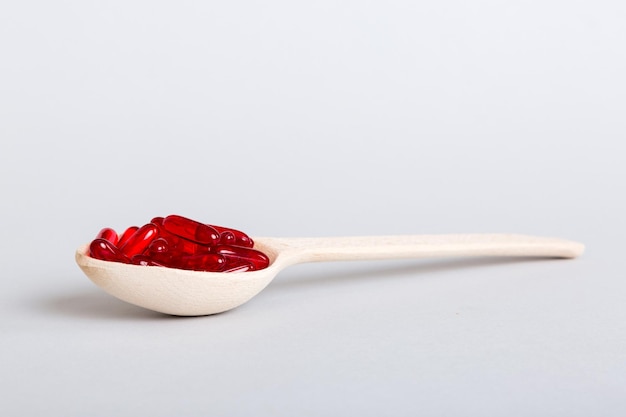 Vitamin capsules in a spoon on a colored background Pills served as a healthy meal Red soft gel vitamin supplement capsules on spoon