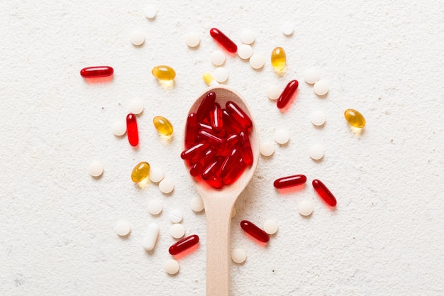 Vitamin capsules in a spoon on a colored background Pills served as a healthy meal Red soft gel vitamin supplement capsules on spoon