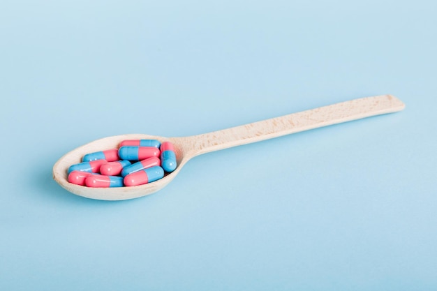 Vitamin capsules in a spoon on a colored background Pills served as a healthy meal Red soft gel vitamin supplement capsules on spoon