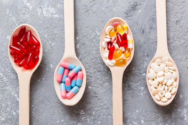 Vitamin capsules in a spoon on a colored background Pills served as a healthy meal Red soft gel vitamin supplement capsules on spoon