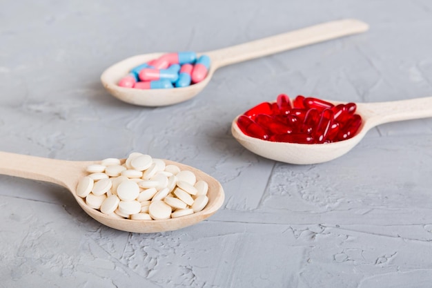 Vitamin capsules in a spoon on a colored background Pills served as a healthy meal Red soft gel vitamin supplement capsules on spoon