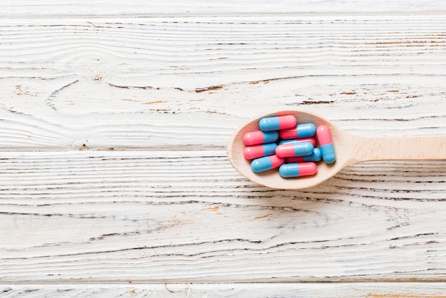 Витаминные капсулы в ложке на цветном фоне Таблетки служат здоровой едой Красные мягкие гелевые капсулы с витаминными добавками на ложке