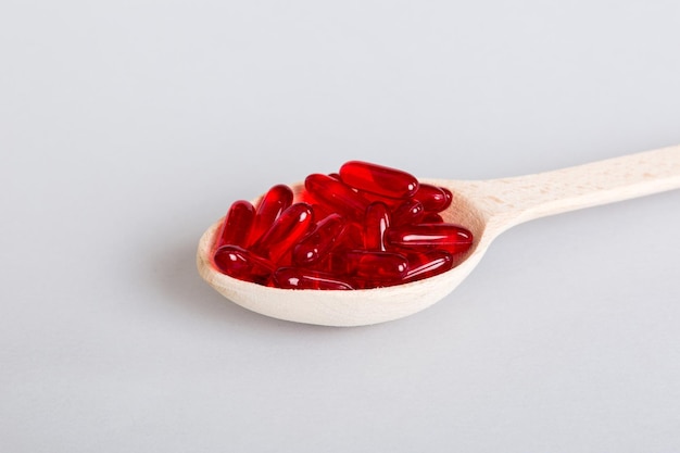 Vitamin capsules in a spoon on a colored background Pills served as a healthy meal Red soft gel vitamin supplement capsules on spoon