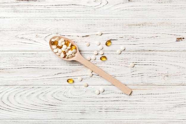 Vitamin capsules in a wooden spoon on a colored background Pills served as a healthy meal Drugs pharmacy medicine or medical healthycare concept